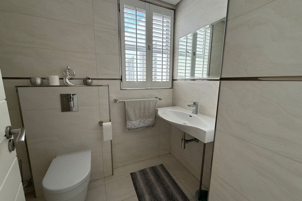 A modern, well-maintained bathroom featuring a wall-mounted toilet with a concealed cistern, a sleek basin, and plantation shutters for privacy.