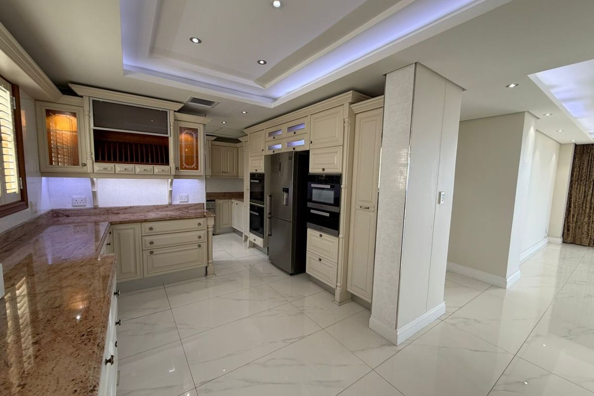 A modern, high-end kitchen featuring granite countertops, extensive built-in cabinetry, integrated appliances, and sophisticated recessed and cove lighting throughout the space.