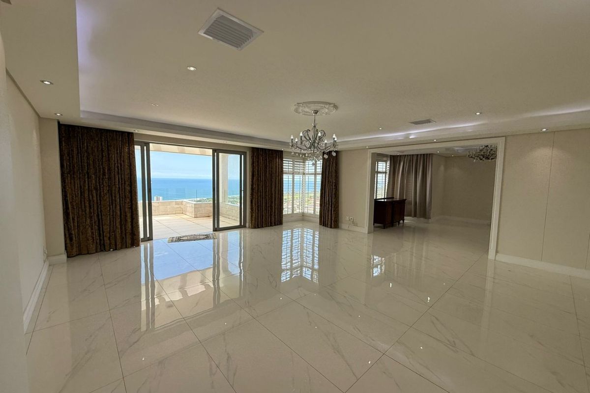 Spacious, light-filled living area featuring polished marble-look floor tiles, recessed lighting, and seamless access to a balcony with ocean views.