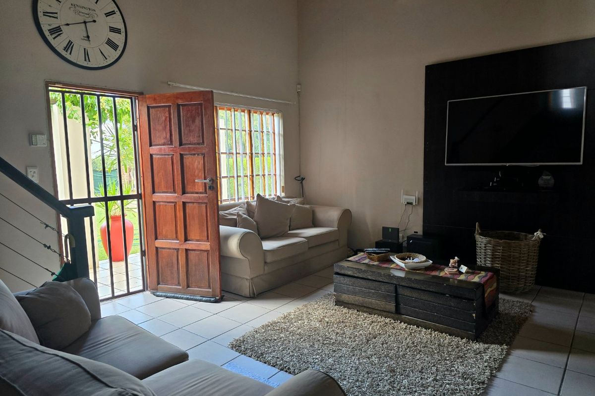 A living room featuring tiled floors, a built-in media wall, and direct access to the garden through a security-gated timber door.