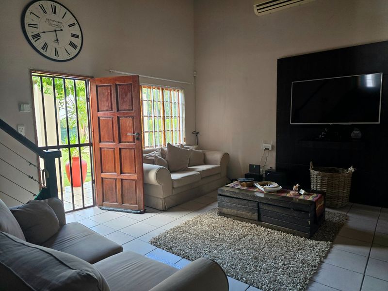 A living room featuring tiled floors, a built-in media wall, and direct access to the garden through a security-gated timber door.