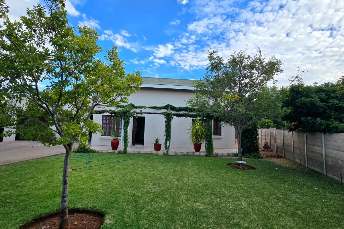 Rear view of the house featuring a paved patio area with a pergola, overlooking a well-maintained garden and lawn.
