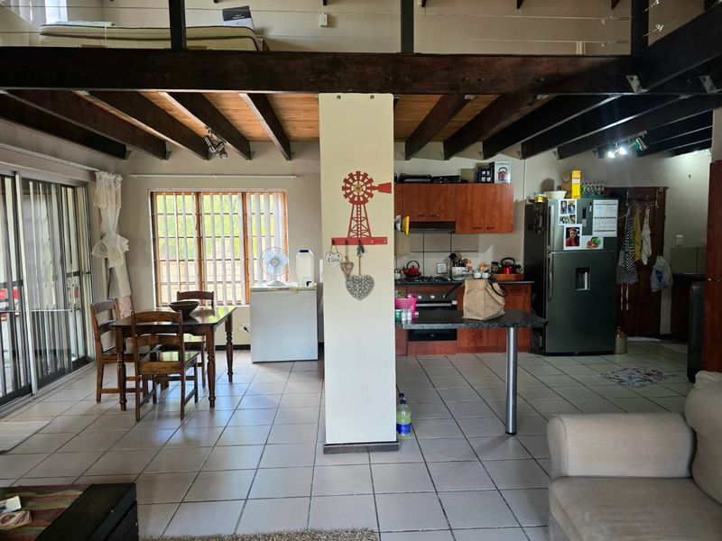 Open-plan living and kitchen area featuring exposed timber beams, tiled flooring, and a mezzanine level, offering a functional layout with potential for modernization.
