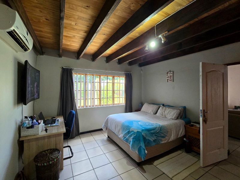 A bedroom featuring exposed timber ceiling beams, tiled flooring, and a wall-mounted air conditioning unit.