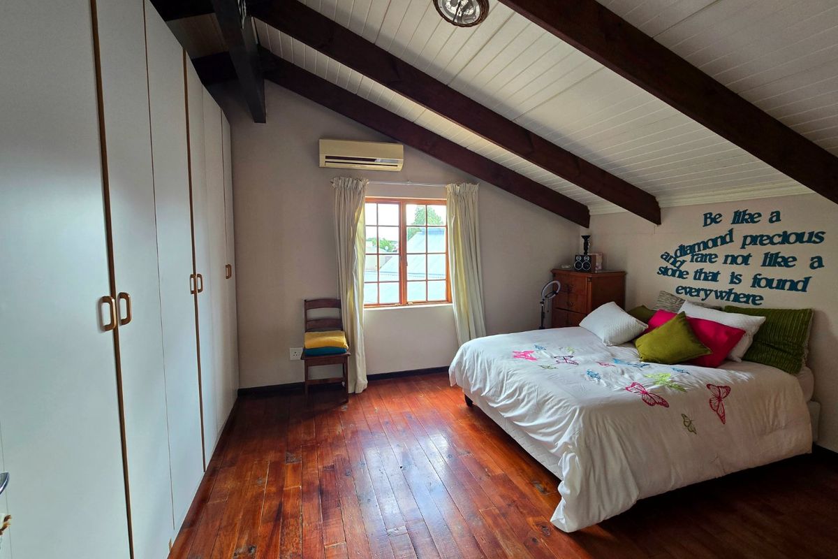 A spacious bedroom featuring warm timber flooring, exposed ceiling beams, built-in wardrobes, and a split-system air conditioner for climate control.