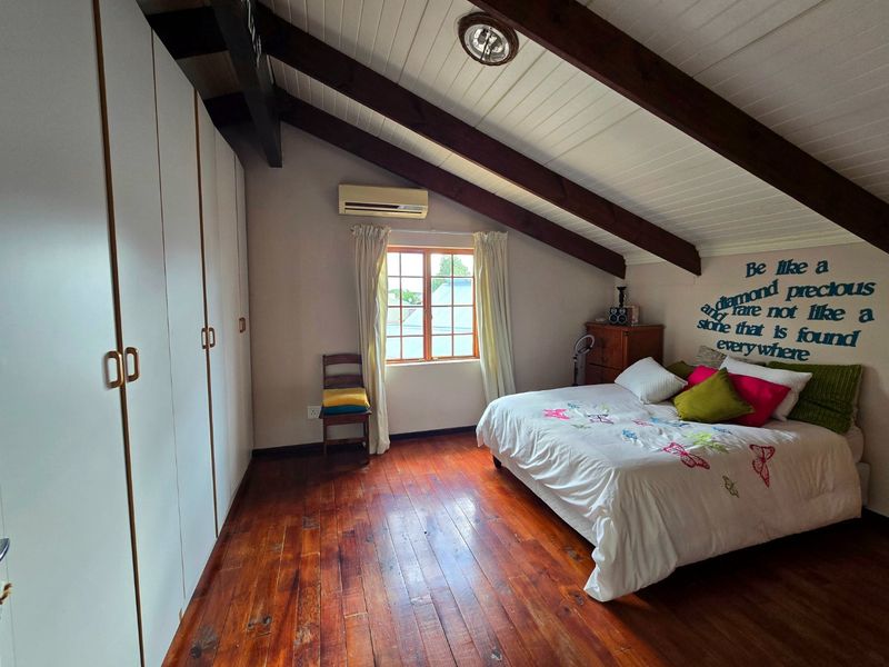 A spacious bedroom featuring warm timber flooring, exposed ceiling beams, built-in wardrobes, and a split-system air conditioner for climate control.