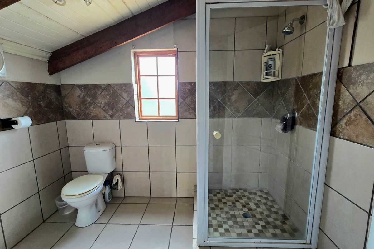 A functional bathroom featuring a shower enclosure, toilet, tiled finishes, and exposed timber ceiling beams under a pitched roof.