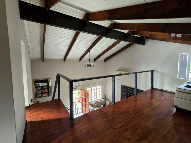 A mezzanine living area featuring vaulted ceilings with exposed timber beams, polished timber flooring, and a modern metal balustrade overlooking the lower level.