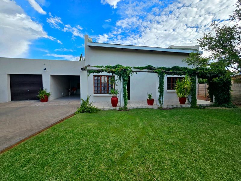 Front view of the house featuring a paved driveway, attached garage, carport, and a covered patio area with a timber pergola overlooking the lawn.