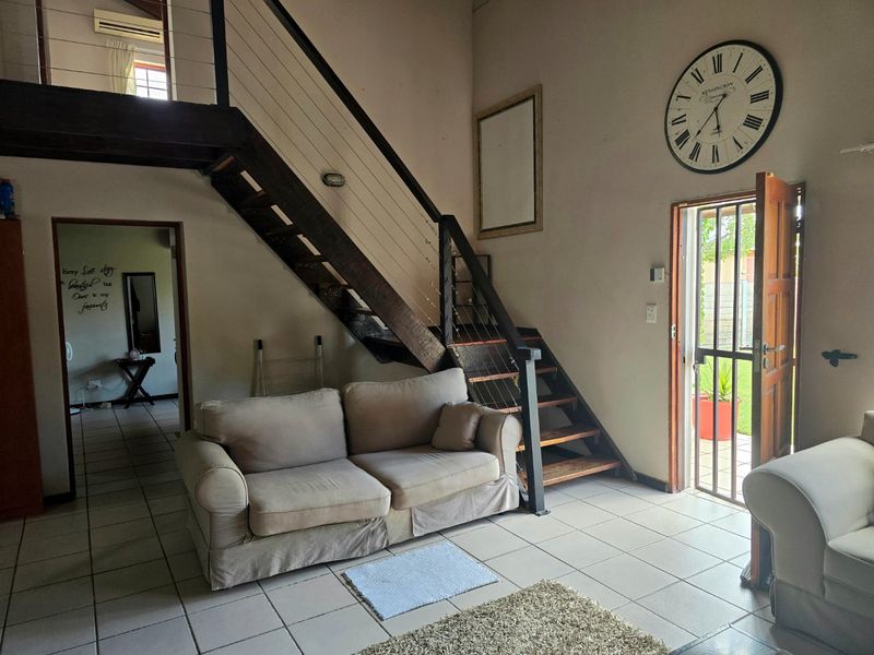 Open-plan living area featuring a timber staircase with cable balustrade, ceramic tiled flooring, and direct access to the exterior via a security gate.