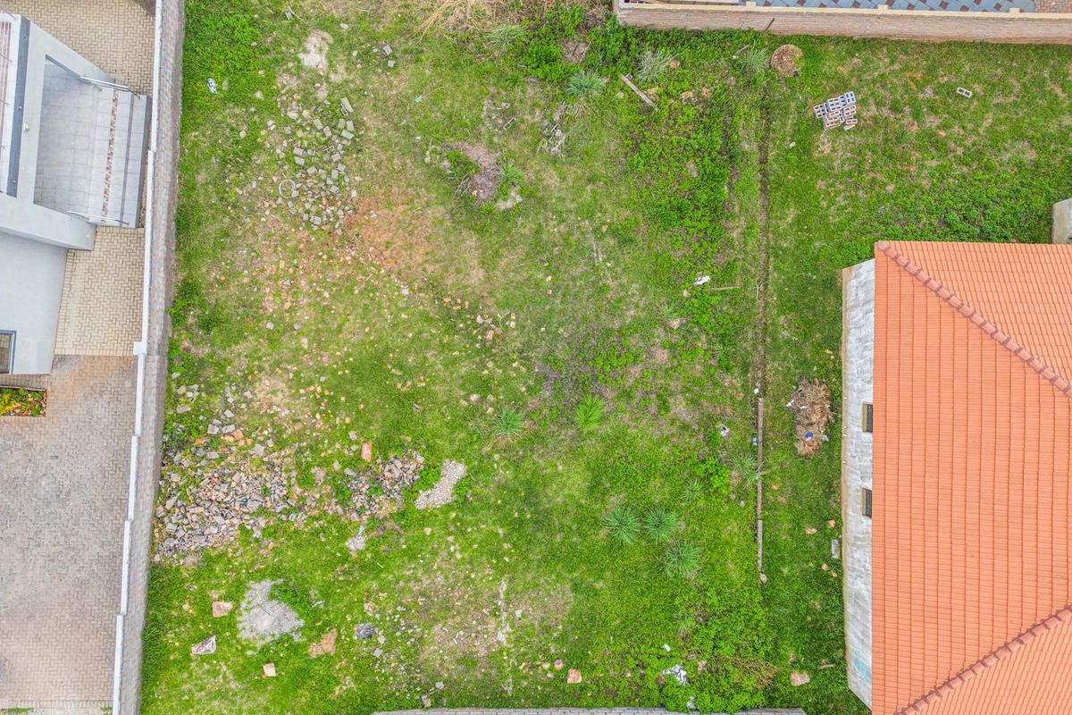 Aerial view of a vacant residential plot featuring boundary walls and grassed terrain, situated between existing neighboring properties.