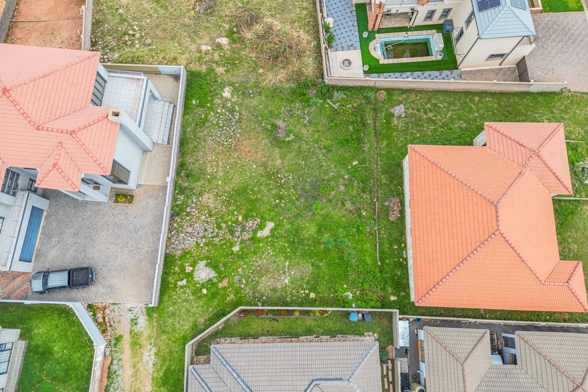 An aerial view of a vacant residential plot situated between established neighboring properties in a suburban estate.