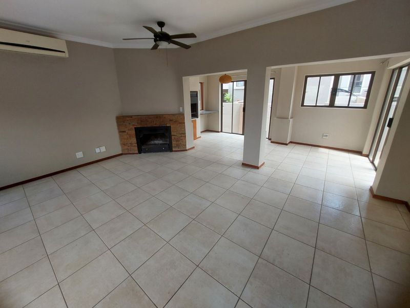 Spacious open-plan living area featuring tiled floors, a stone-clad fireplace, ceiling fan, and split-system air conditioning, with direct access to outdoor space.