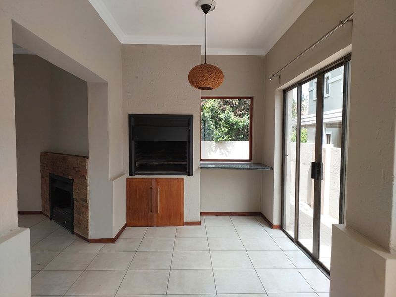 Covered patio area featuring a built-in braai, brick fireplace, tiled flooring, and sliding glass doors providing access to the exterior.