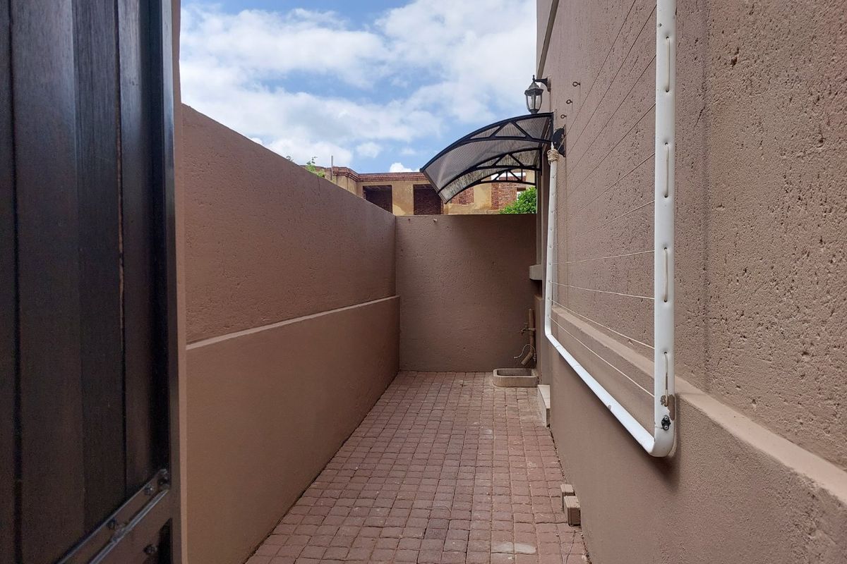 A narrow, paved side passage featuring a wall-mounted washing line, an exterior light fixture, and a small fixed awning over the outdoor tap area.