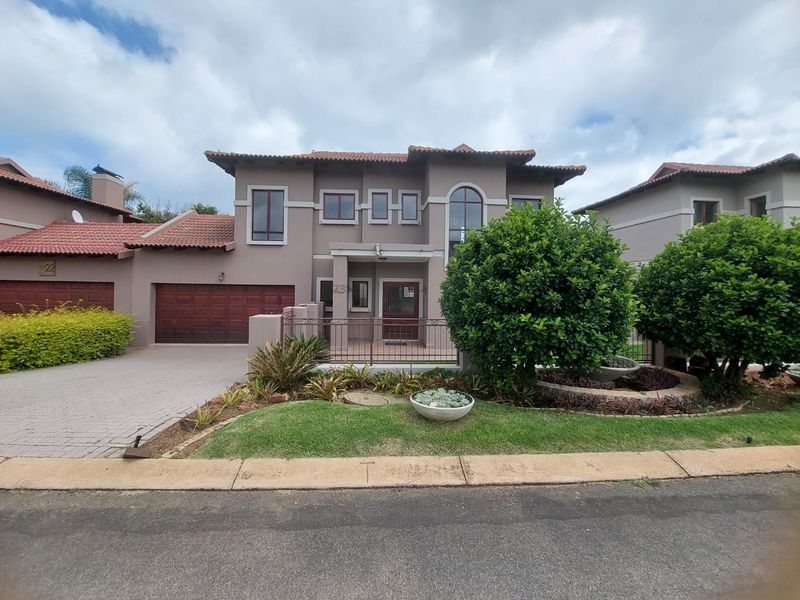 Front elevation of a two-story residential house featuring a tiled roof, double garage, paved driveway, and a well-maintained landscaped garden.