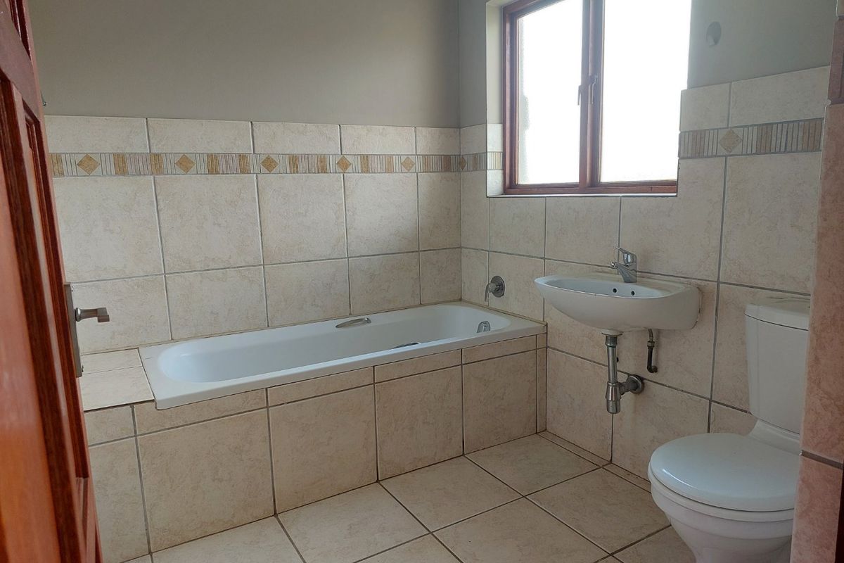 A functional bathroom featuring a built-in bathtub, wall-mounted basin, and toilet with neutral ceramic tiling throughout.