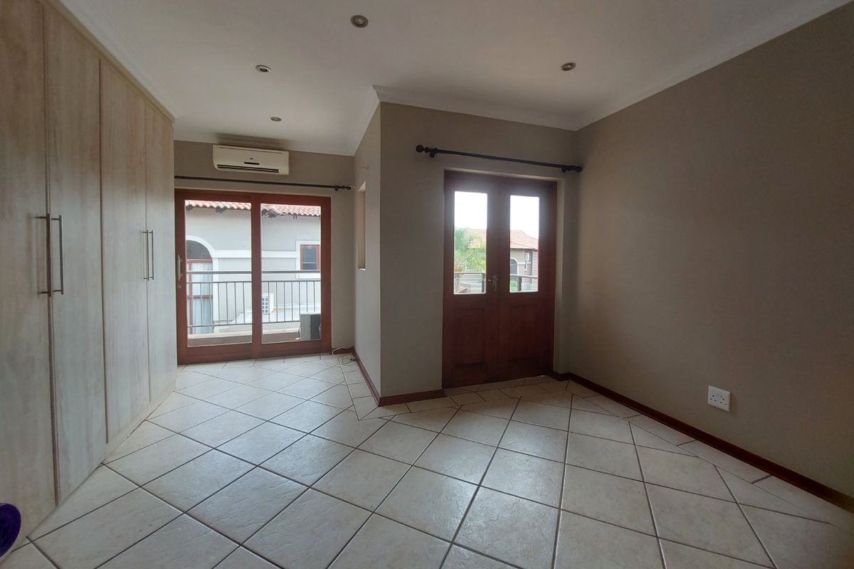 A spacious, empty bedroom featuring neutral tiled flooring, built-in cupboards, an air conditioning unit, and direct access to an outdoor balcony area.