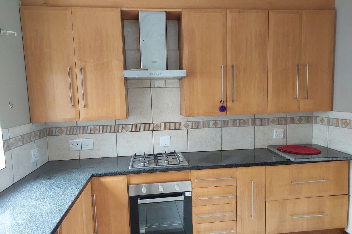 A functional kitchen featuring wooden cabinetry, granite countertops, a built-in oven, gas hob, and a stainless steel extractor fan with a tiled backsplash.
