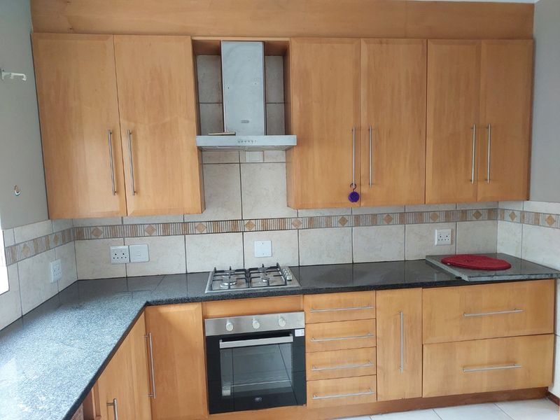 A functional kitchen featuring wooden cabinetry, granite countertops, a built-in oven, gas hob, and a stainless steel extractor fan with a tiled backsplash.