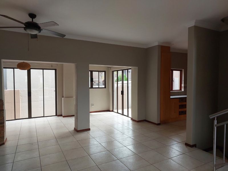Spacious open-plan living area featuring neutral tiled flooring, ceiling fan, and multiple sliding glass doors providing access to the exterior.