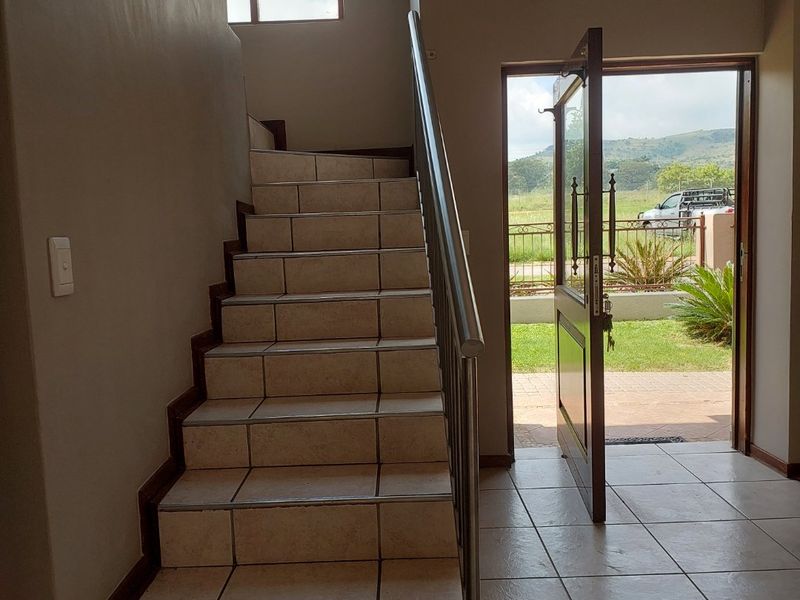 Bright entrance hall featuring a tiled staircase with a metal handrail, leading to an open-plan area with direct access to the exterior.