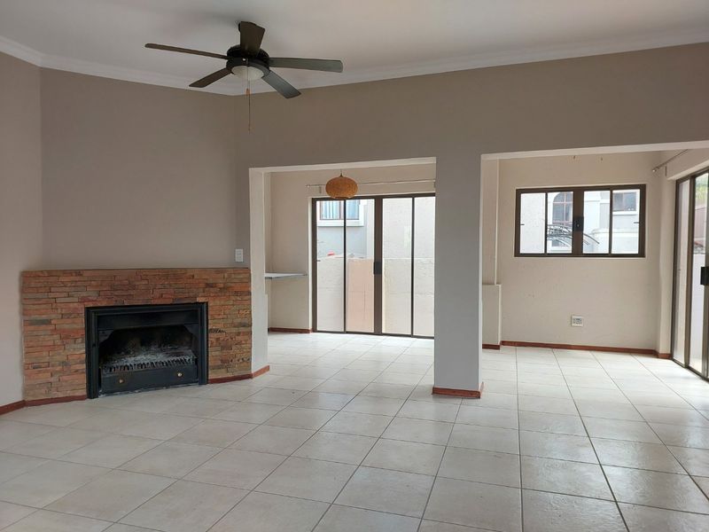 Spacious open-plan living area featuring a brick fireplace, tiled flooring, ceiling fan, and large sliding doors providing access to the exterior.