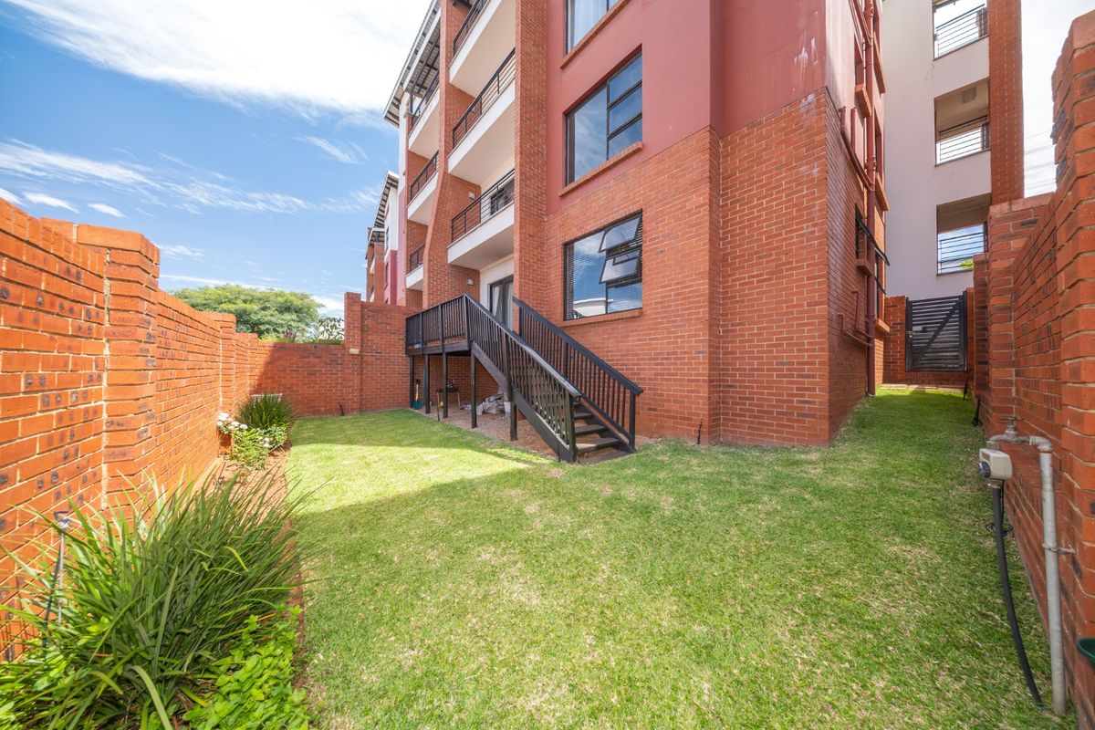 A private rear garden featuring a well-maintained lawn, brick boundary walls, and a raised timber deck with stairs leading to the townhouse unit.