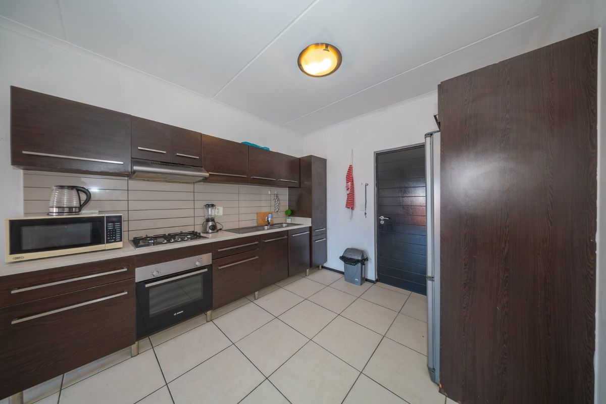 A functional kitchen featuring dark wood cabinetry, built-in oven, gas hob, extractor fan, and tiled flooring with a neutral backsplash.