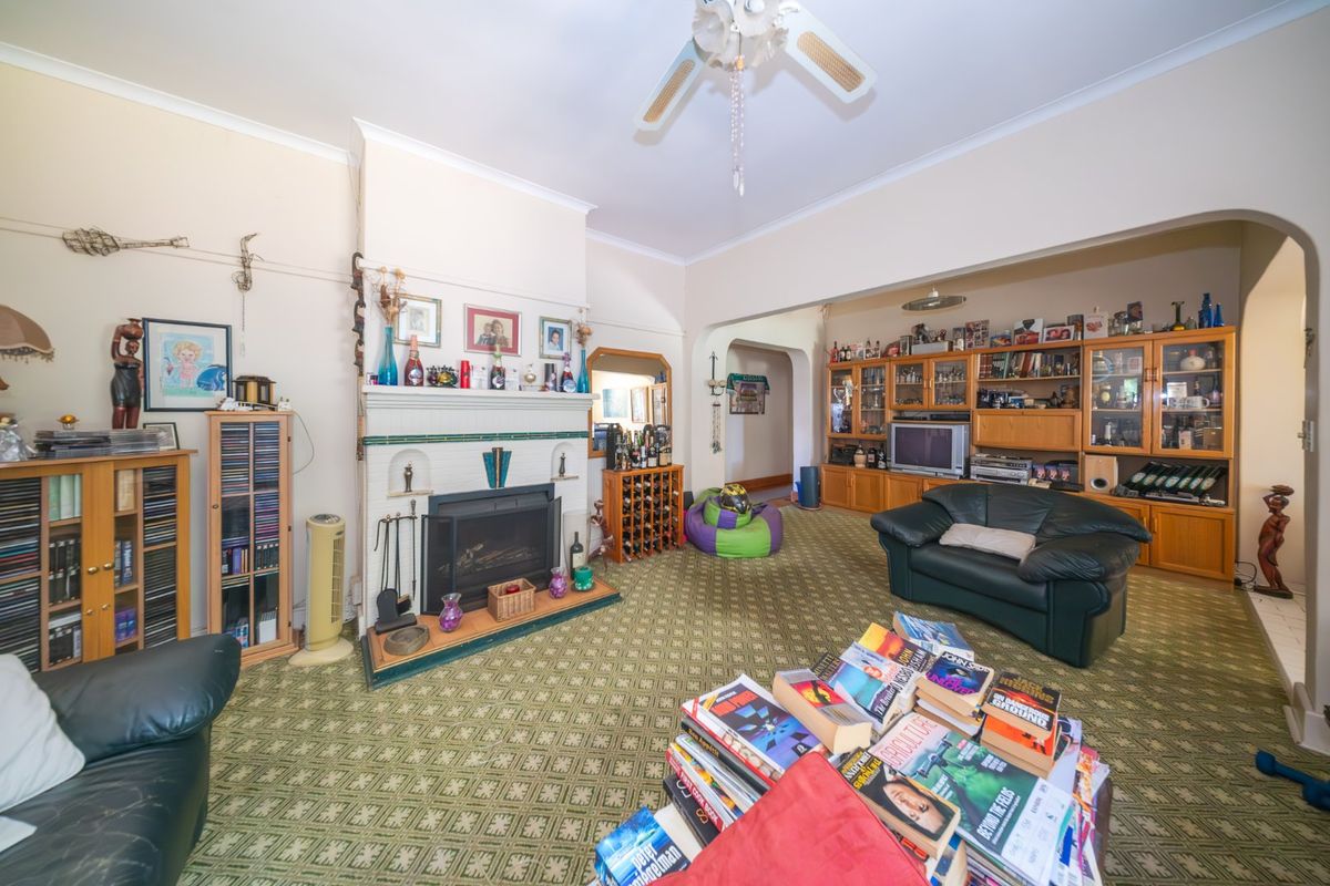 Spacious living room featuring a traditional fireplace, built-in cabinetry, and a ceiling fan, offering a classic layout with potential for modern updates.