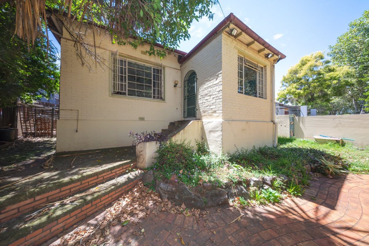 Rear exterior view of a brick house featuring a paved patio area, stone retaining wall, and security-gated entrance with steps.