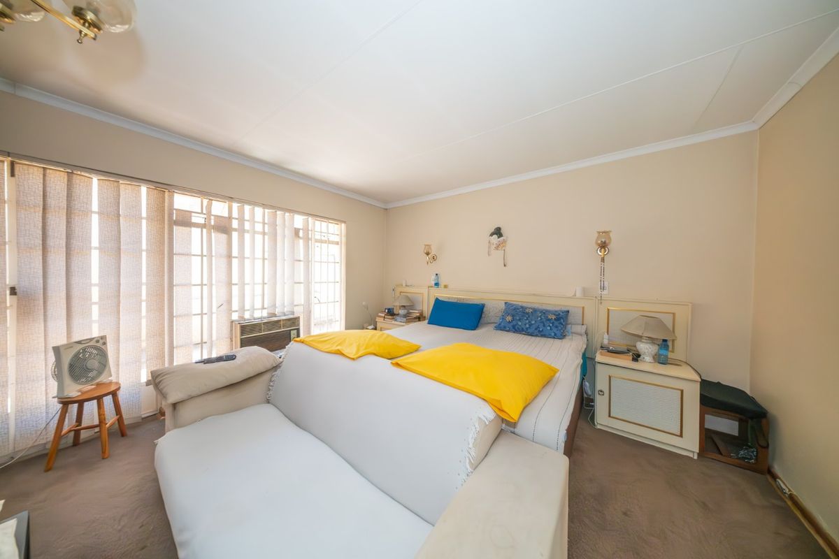 A bedroom featuring built-in headboard and bedside cabinetry, vertical blinds, and a window-mounted air conditioning unit.