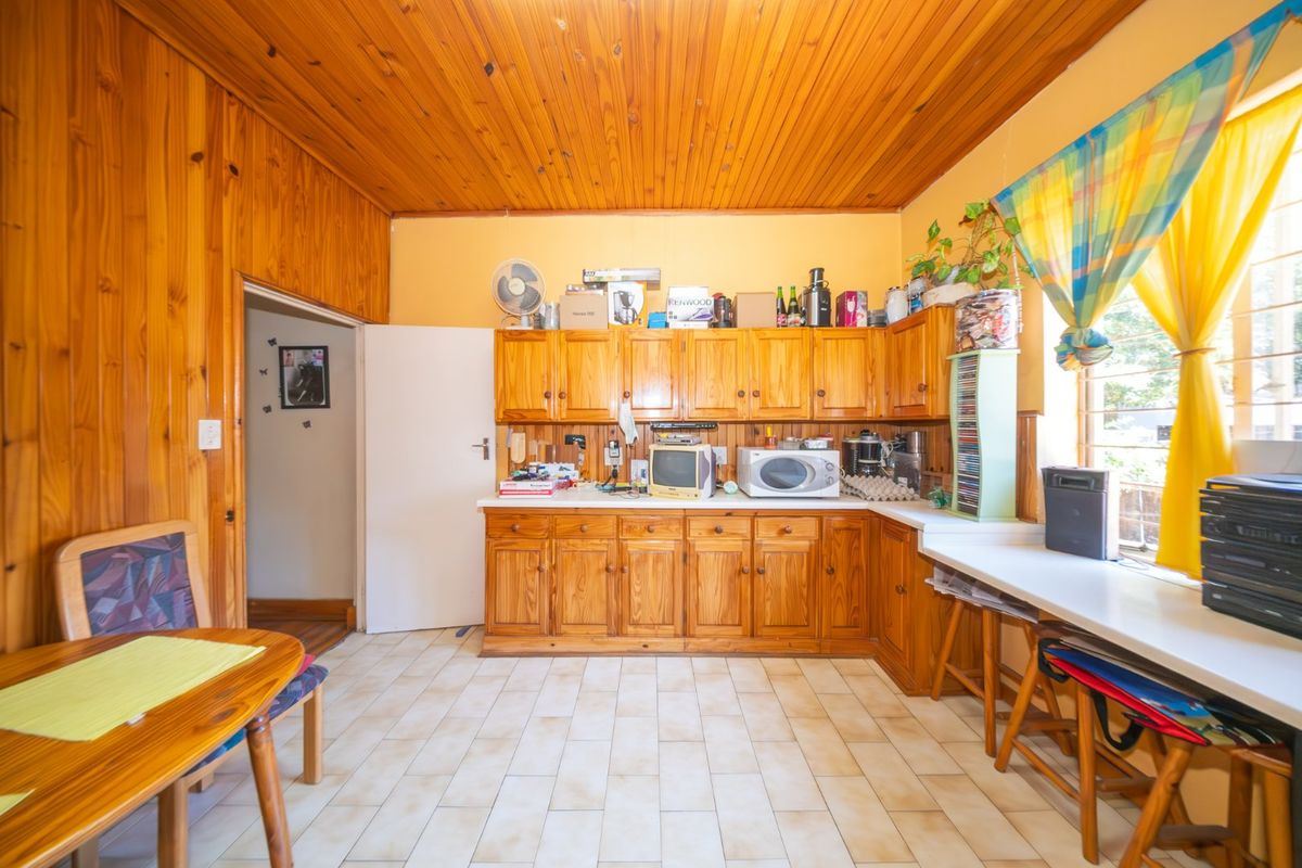 A dated kitchen featuring extensive timber wall and ceiling paneling, traditional wooden cabinetry, and tiled flooring, offering significant potential for a modern renovation.