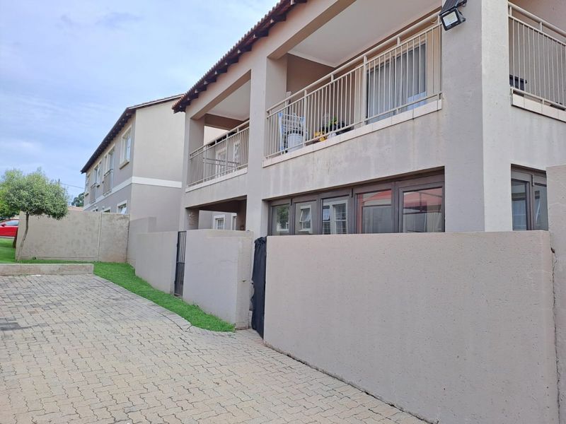 Front exterior view of a multi-story residential building featuring a paved driveway, boundary wall, and upper-level balconies with metal railings.