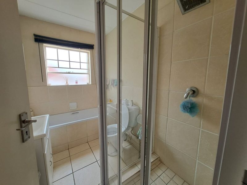 A functional bathroom featuring a shower enclosure, bathtub, toilet, and vanity basin with neutral wall and floor tiling.