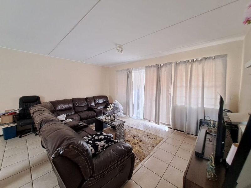 A spacious living room featuring neutral wall tones, ceramic floor tiles, and a large sliding glass door providing access to the exterior.