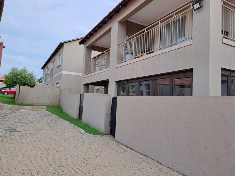 Rear view of a multi-story residential building featuring a paved driveway, boundary wall, and upper-level balconies with metal railings.