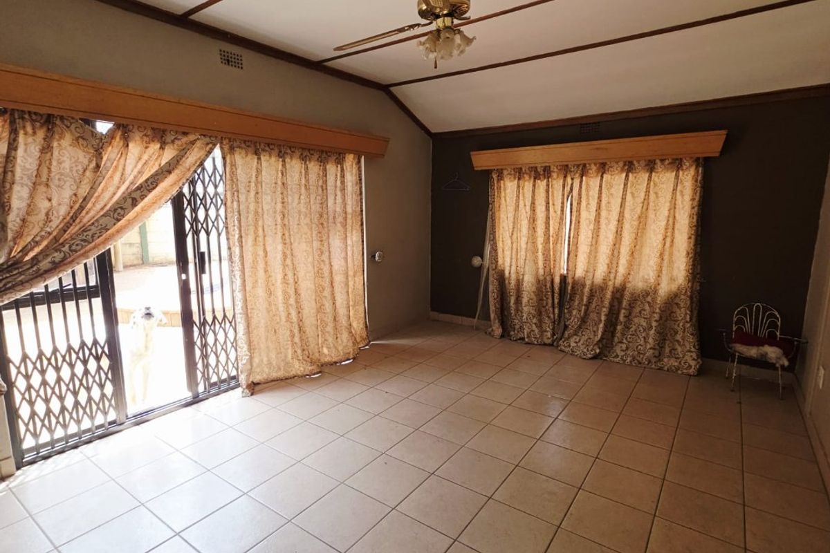 Spacious living area featuring tiled flooring, a ceiling fan, and large sliding glass doors with security gates leading to the exterior.