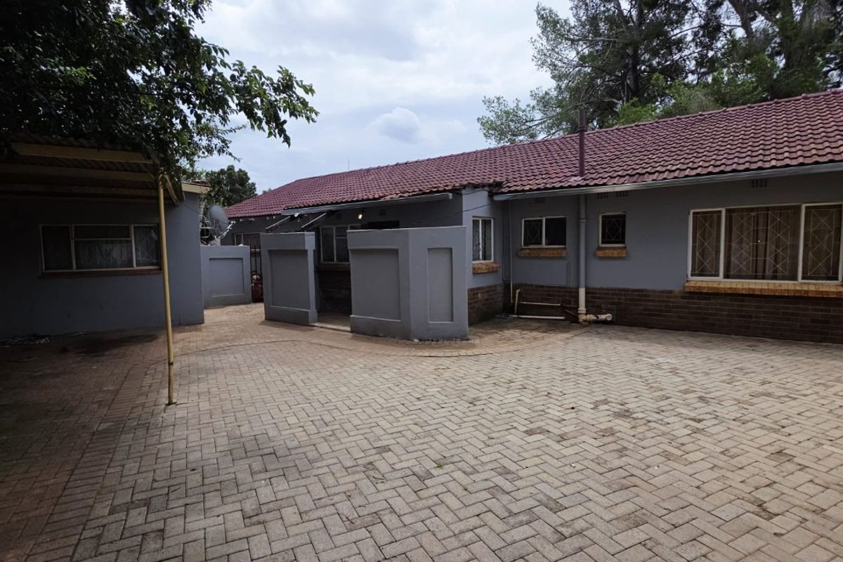 Rear exterior view of the property featuring a paved courtyard, brick and painted facade, and a tiled roof with an attached carport.