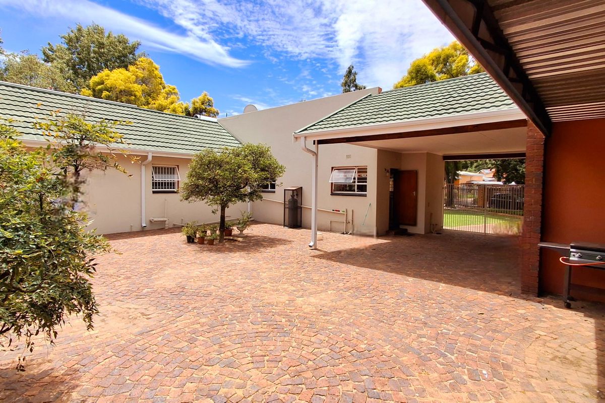 A spacious brick-paved rear courtyard featuring a covered carport area, well-maintained exterior walls, and a tiled roof structure.