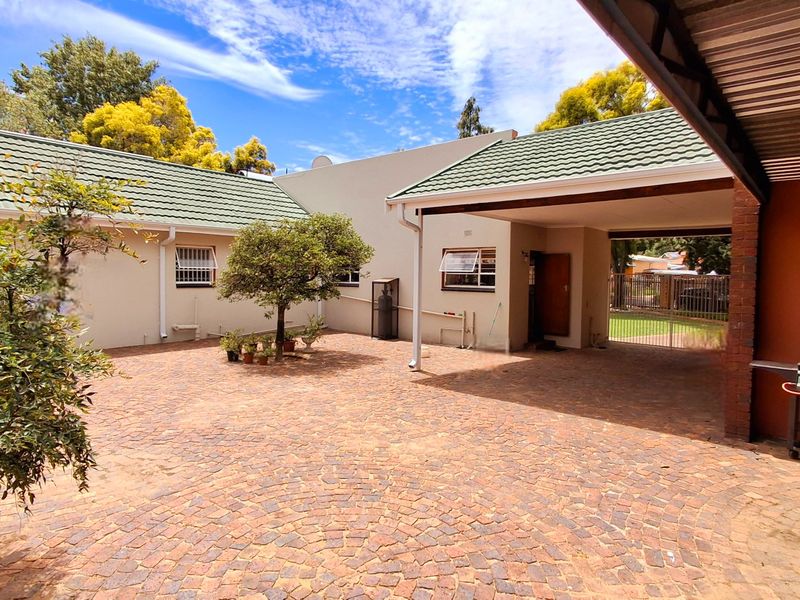 A spacious brick-paved rear courtyard featuring a covered carport area, well-maintained exterior walls, and a tiled roof structure.