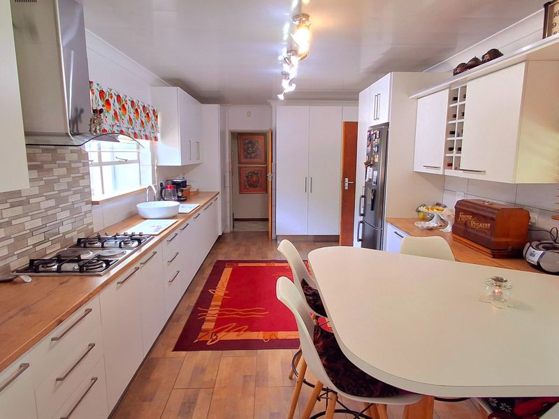 A well-maintained kitchen featuring white cabinetry, wooden countertops, a gas hob, stainless steel extractor fan, and integrated storage solutions.