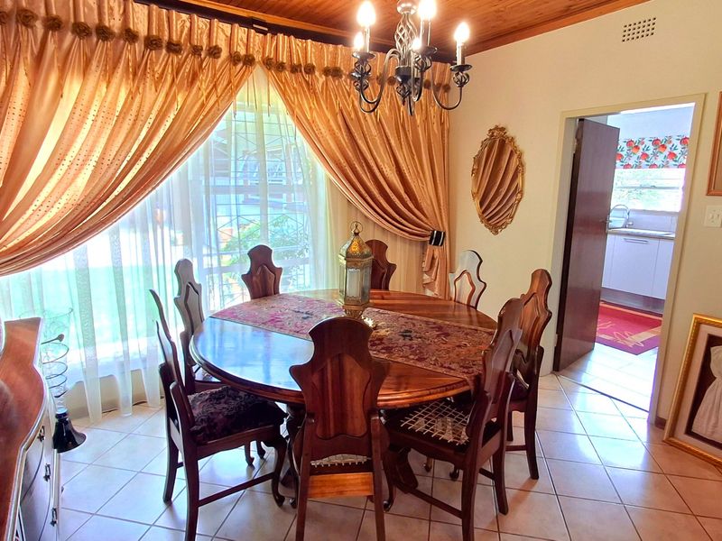 A traditional dining room featuring ceramic floor tiles, a timber ceiling, and a decorative wrought iron chandelier, with direct access to the kitchen area.