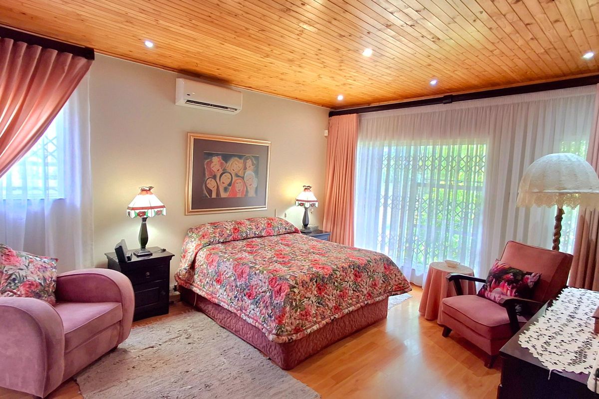 Spacious bedroom featuring a warm timber-paneled ceiling, laminate flooring, and direct access to the outdoors via a sliding glass door with a security gate.