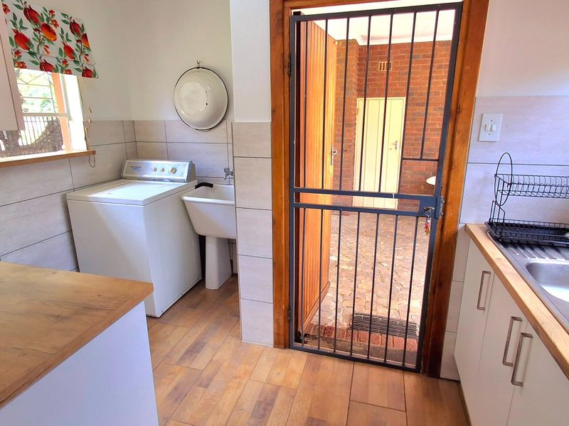 Functional laundry area featuring laminate flooring, tiled splashbacks, a utility sink, and direct access to an outdoor courtyard through a security gate.
