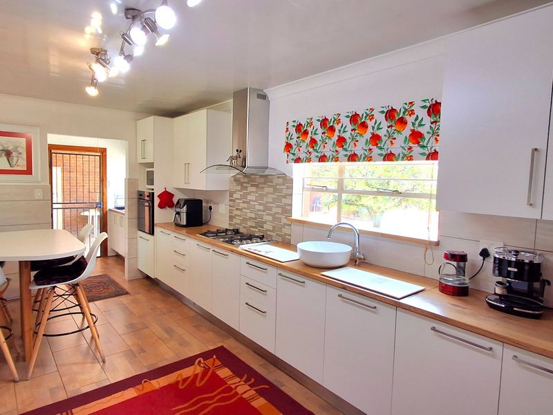 Modern kitchen featuring white cabinetry, wooden countertops, gas hob, extractor fan, and integrated oven, with a breakfast bar area and tiled flooring.