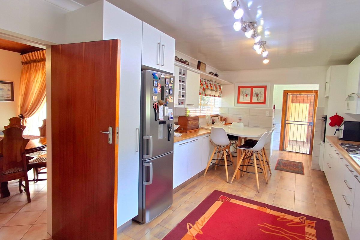 A functional kitchen featuring white cabinetry, a gas hob, extractor fan, and tiled flooring, with an adjacent dining area visible through the doorway.