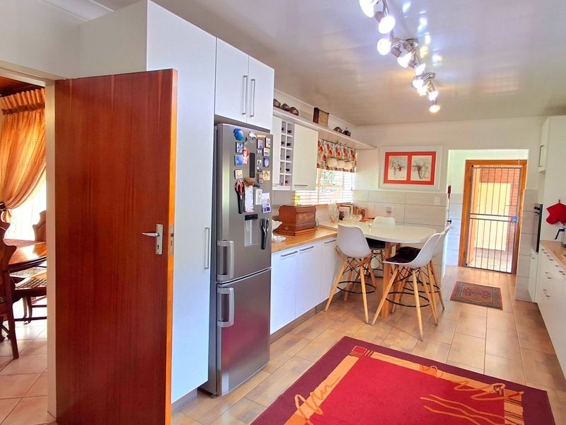A functional kitchen featuring white cabinetry, a gas hob, extractor fan, and tiled flooring, with an adjacent dining area visible through the doorway.