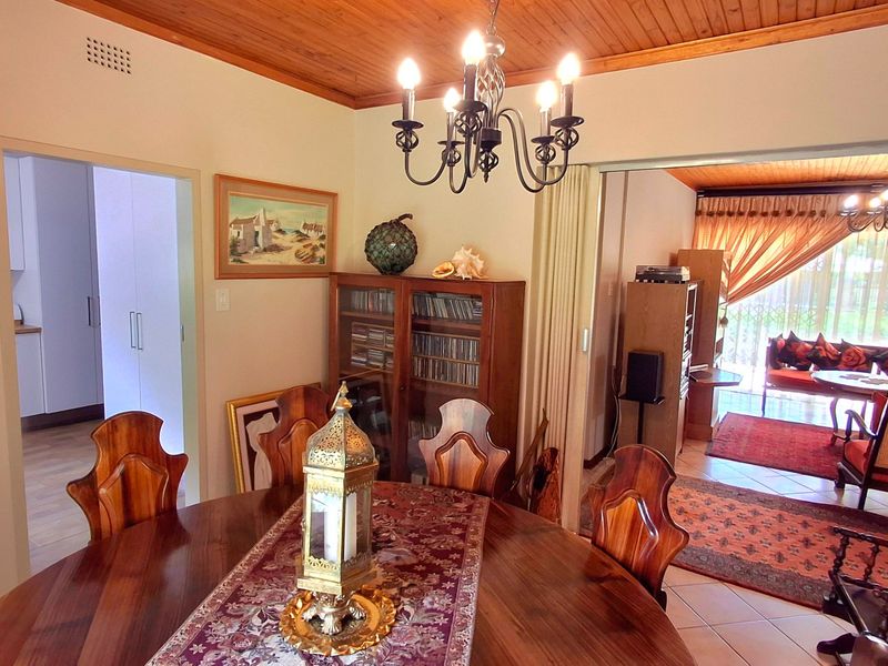Dining room featuring a timber ceiling, wrought iron chandelier, and tiled flooring, with an open-plan flow into the adjacent living area.