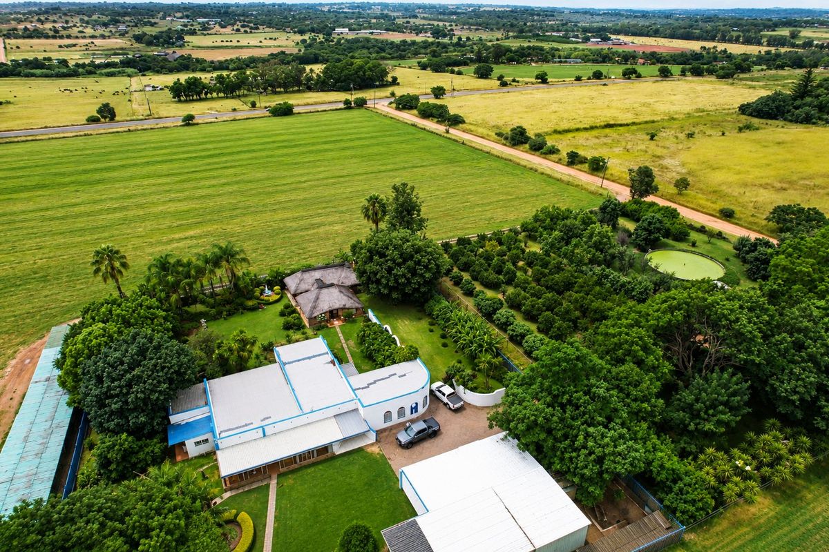 Aerial view of a farm property featuring a main residence with metal and thatched roofing, outbuildings, a swimming pool, and extensive surrounding agricultural land.